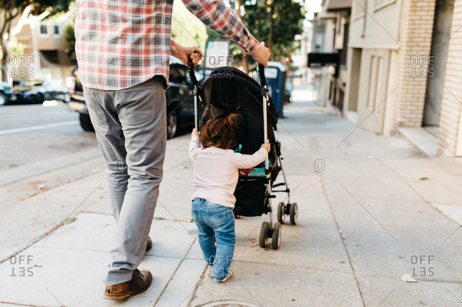 Toddler helping father push stroller while out for a walk together