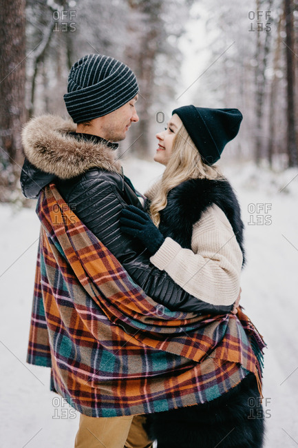married beautiful couple hugging looking at each other in the winter forest throwing warm checkered blanket