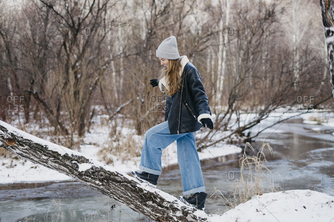 beautiful woman goes and balances the tree and looks at his feet. on the background of winter forest and river