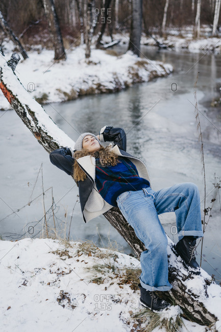 beautiful woman lies on a tree and looks at the sky. on the background of winter forest and river