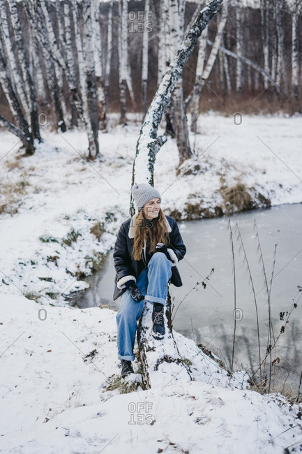 beautiful girl sitting on a tree background of a winter forest and river