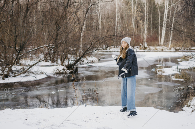beautiful girl throws a snowball at a friend in the background of winter forest and river