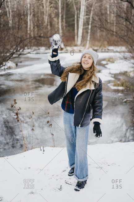 beautiful girl throws a snowball at a friend in the background of winter forest and river