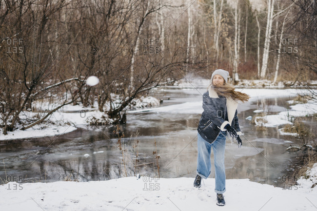 beautiful girl throws a snowball at a friend in the background of winter forest and river