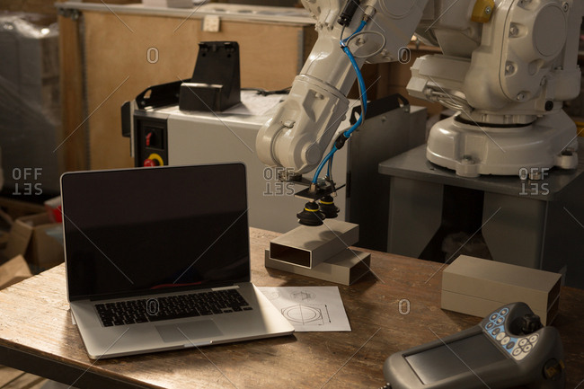 Laptop, robotic machine and remote control on table in warehouse