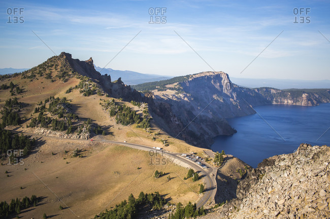 View looking down on a mountain road curving along an exposed ridgeline above a deep blue lake, Crater Lake, Oregon, USA