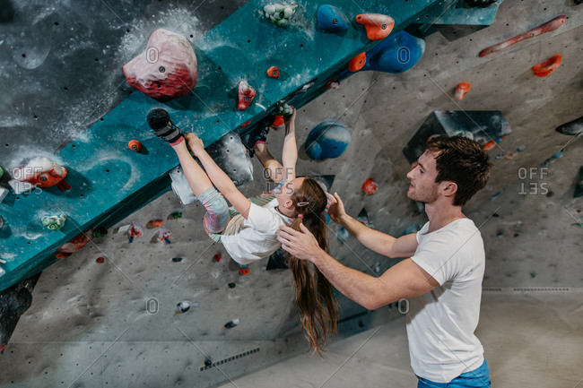 Bouldering trainer helping a child climb up an artificial climbing wall. Child learning to climb up a bouldering wall with a coach in an indoor bouldering gym.
