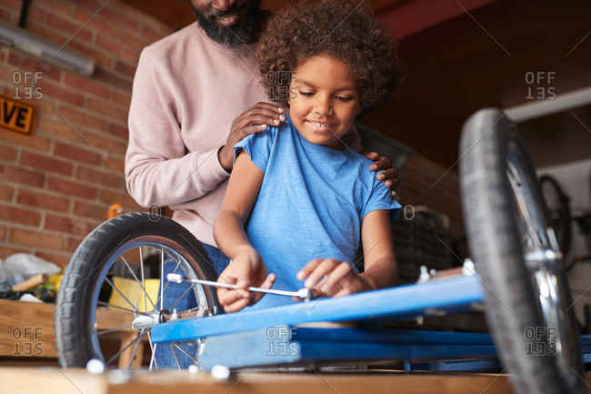 Low angle view of pre-teen boy standing at a workbench making a racing kart, with his father standing behind him helping, low angle close up, selective focus