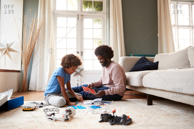 Pre-teen boy sitting on the floor in the sitting room with his father, following instructions for a toy construction kit together, full length