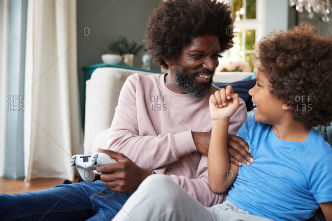 Happy pre-teen boy and his father sitting on the floor in the living room laughing and playing video games together,  close up