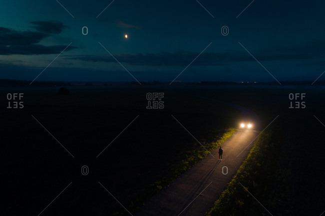 Aerial view of man standing on road at night with waning moon, Estonia
