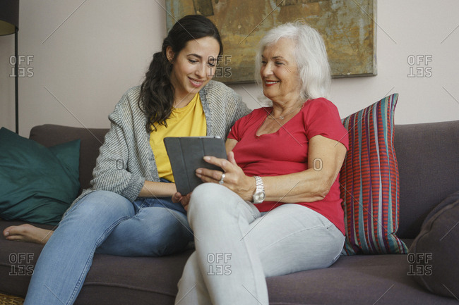 Senior mother and daughter using digital tablet on living room sofa