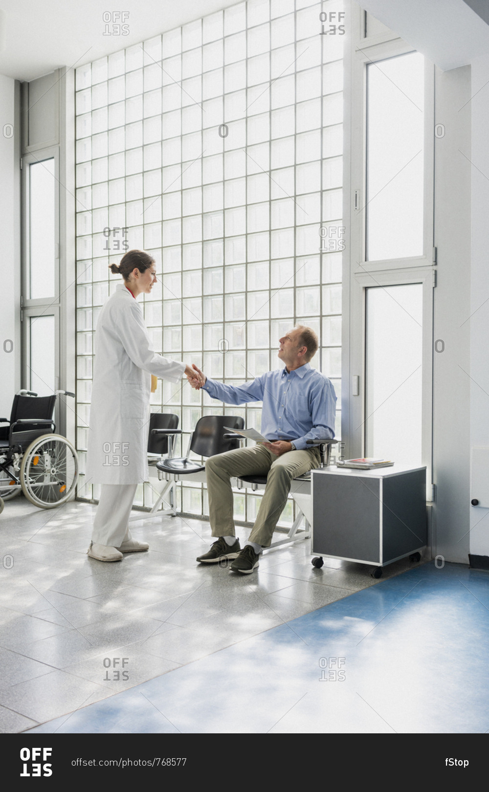 Doctor greeting, shaking hands with patient in clinic waiting room