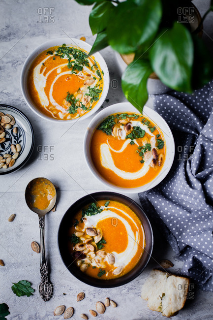 Bowls of homemade squash soup garnished with chopped cilantro and roasted pumpkin seeds