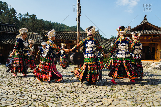 GUINZHOU, CHINA - JUNE 14, 2018: Females of Miao ethnic group in bright costumes with colorful ornaments and headdresses performing traditional festival dance on village square on sunny summer day in Guizhou province of China