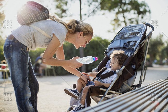 Mother giving water bottle to his son- sitting in pram