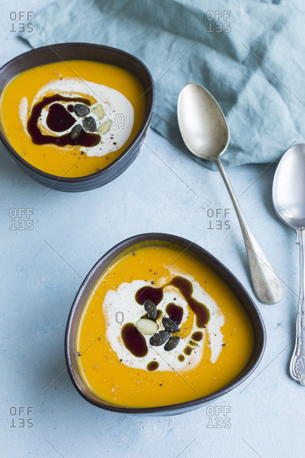 Two bowls of homemade Hokkaido pumpkin soup garnished with cream- pumpkin seed oil and pumpkin seed
