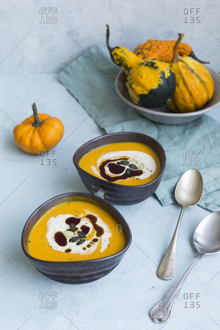 Two bowls of homemade Hokkaido pumpkin soup garnished with cream- pumpkin seed oil and pumpkin seed