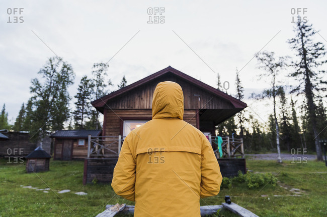 Man standing in front of log cabin- rear view