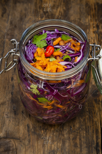 Homemade red cabbage- fermented- with chili- carrot and coriander- preserving jar on wood