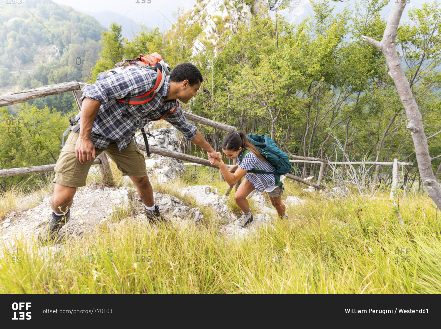 Italy- Massa- man helping a young woman to climb a step while hiking in the Alpi Apuane mountains