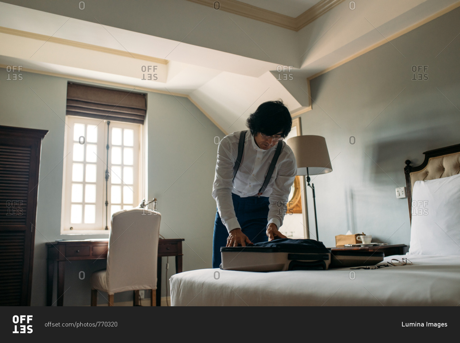 Asian man hotel guest packing his clothes in suitcase.