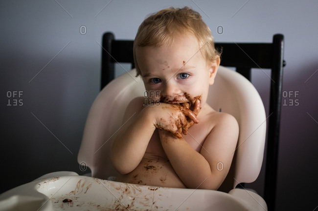 Toddler boy making mess with chocolate in high chair