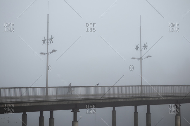 Person walking across bridge on a foggy day