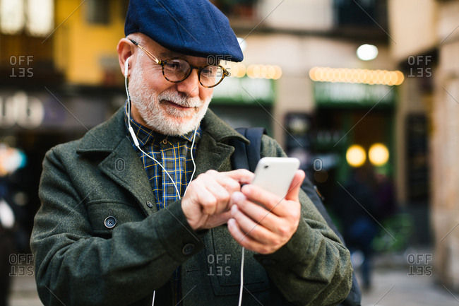 Senior man wearing beret using his phone on the street.