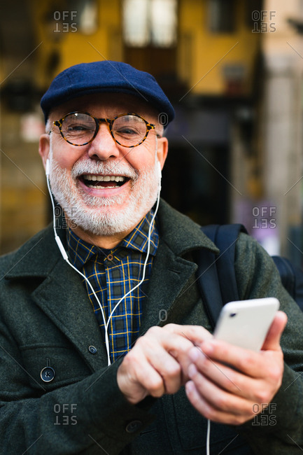Happy senior man wearing beret using his phone on the street.