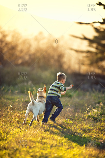 Little boy running on the field with his dog.