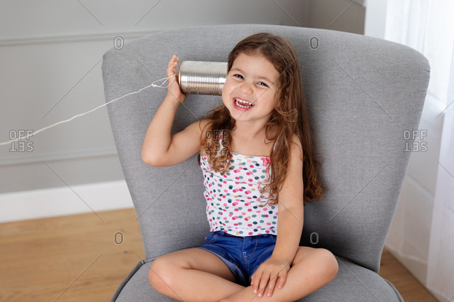 Laughing girl sitting on chair listening to toy telephone made with tin can and string