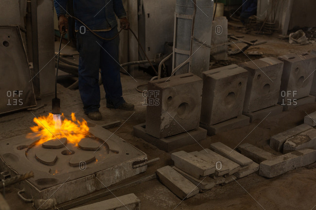 Low section of worker heating metal casting with flaming torch