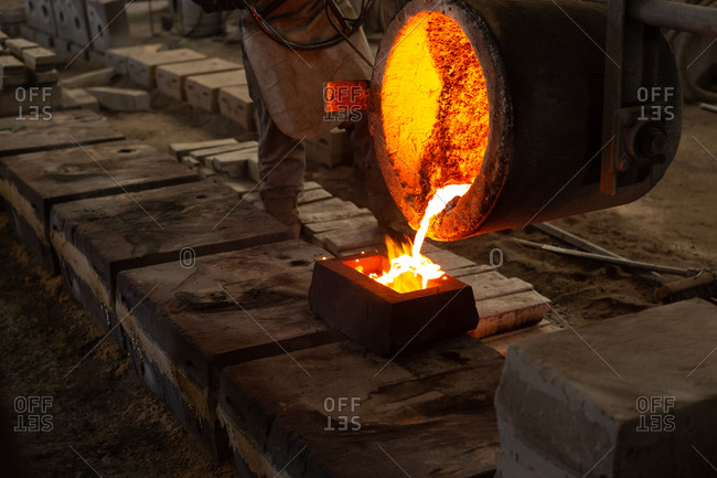 Worker pouring molten metal from flasks into molds in foundry
