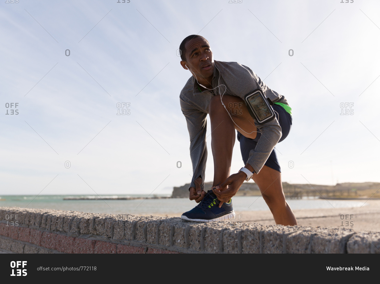 Male athlete tying his shoelaces on surrounding wall at beach