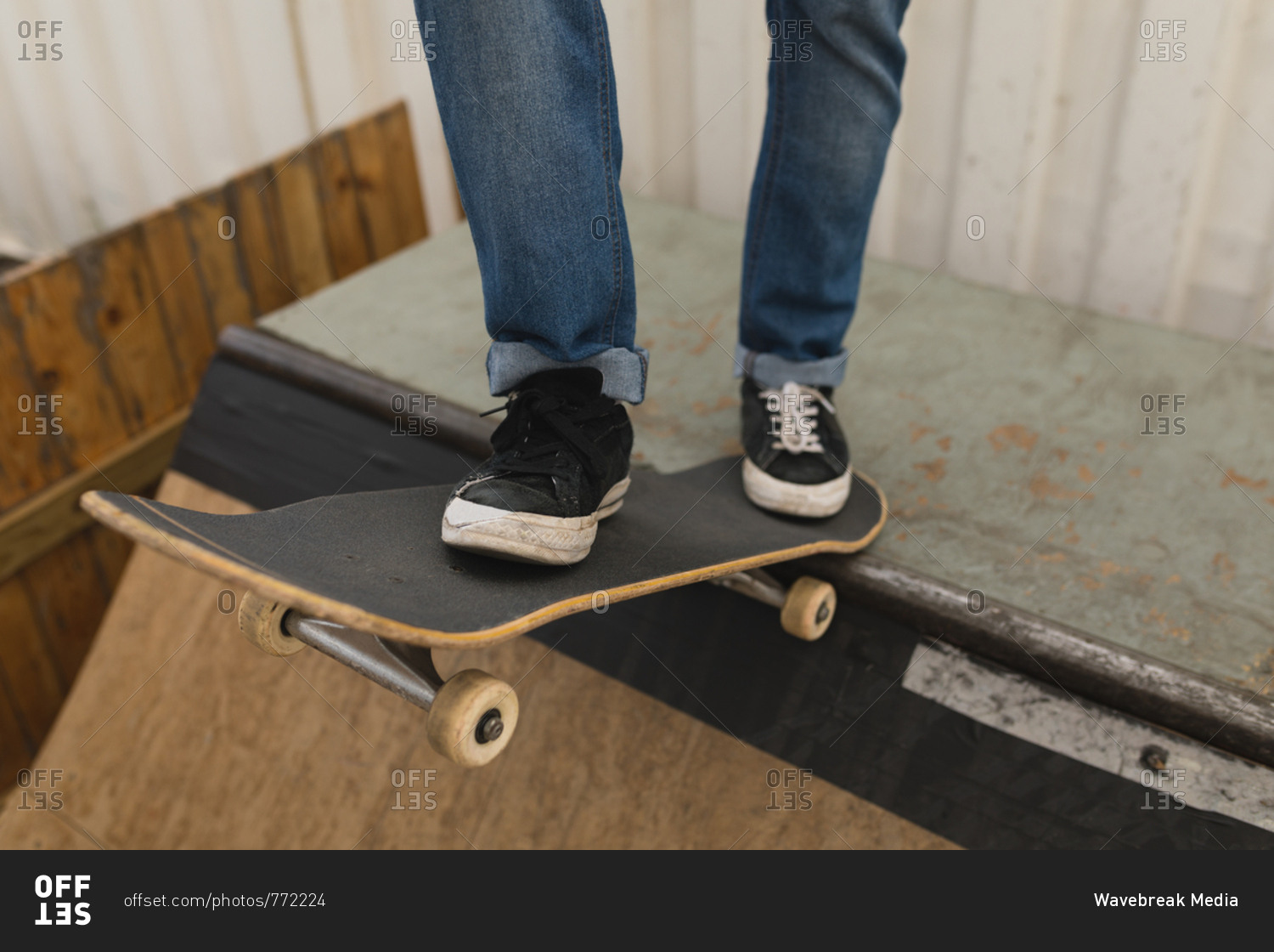 Low section of skateboarder standing with skateboard on skateboard ramp at skateboard court