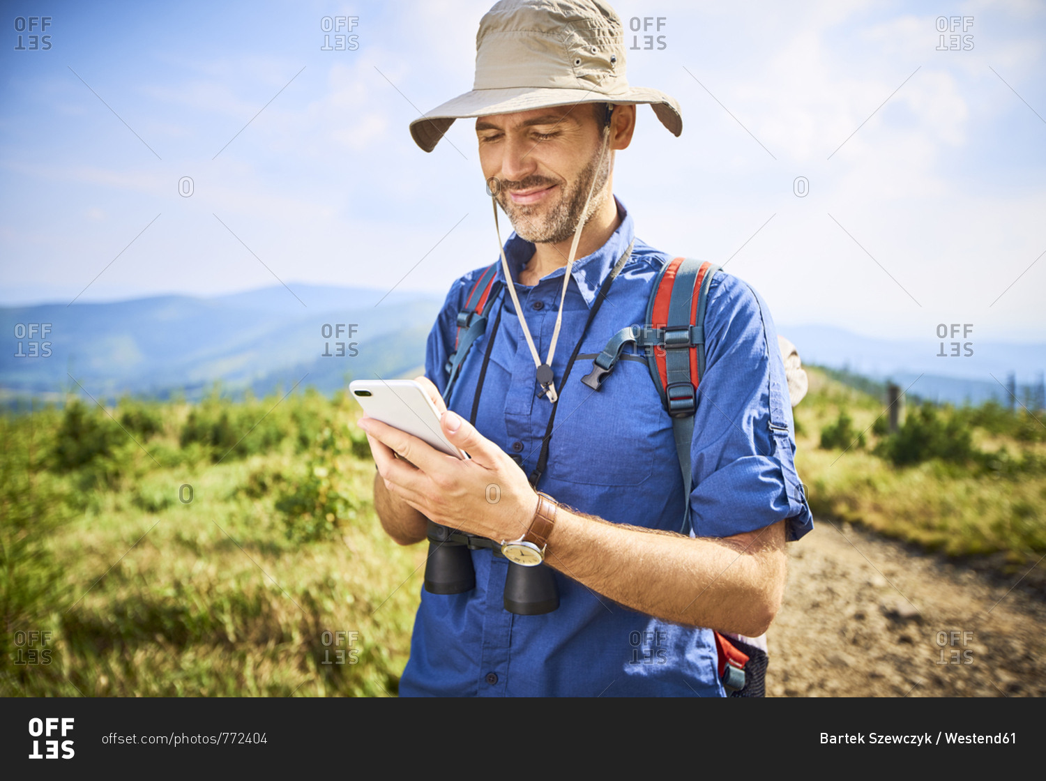 Smiling man checking his cell phone during hiking trip