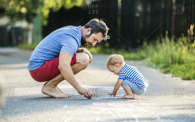 Father and his little daughter drawing with chalks on street in summer