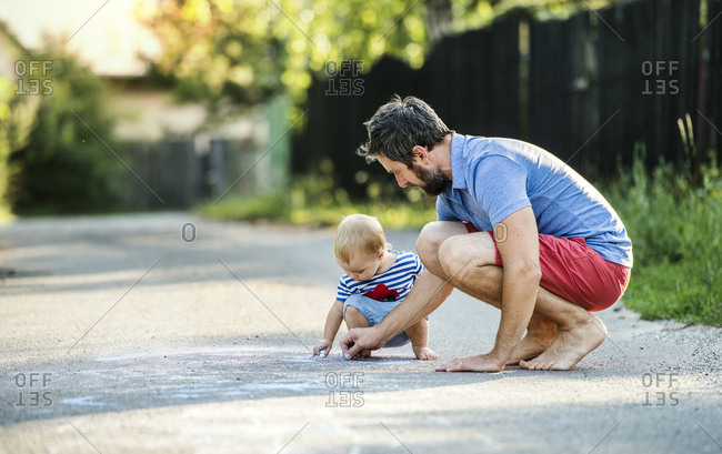 Father and his little daughter drawing together with chalks on street in summer