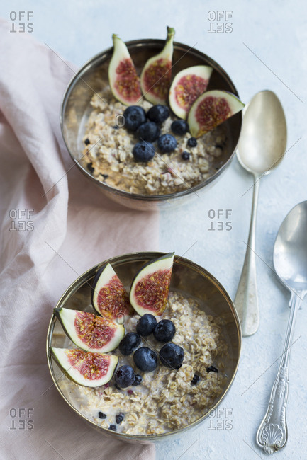 Two bowls of porridge with sliced figs- blueberries and dried berries