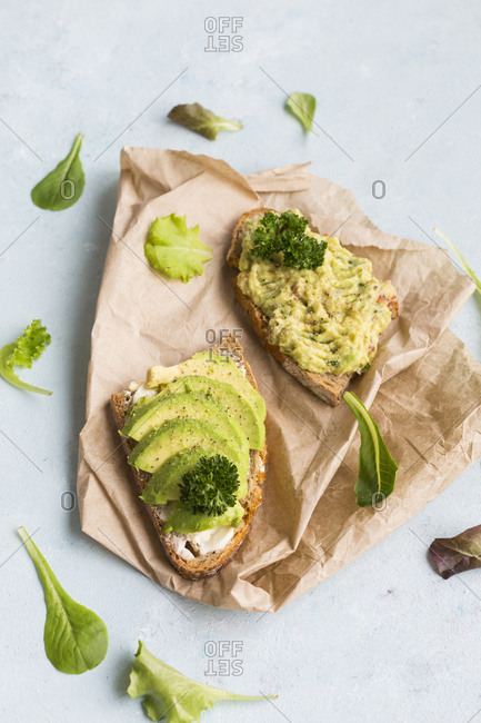 Slices of bread with sliced avocado and avocado cream on brown paper
