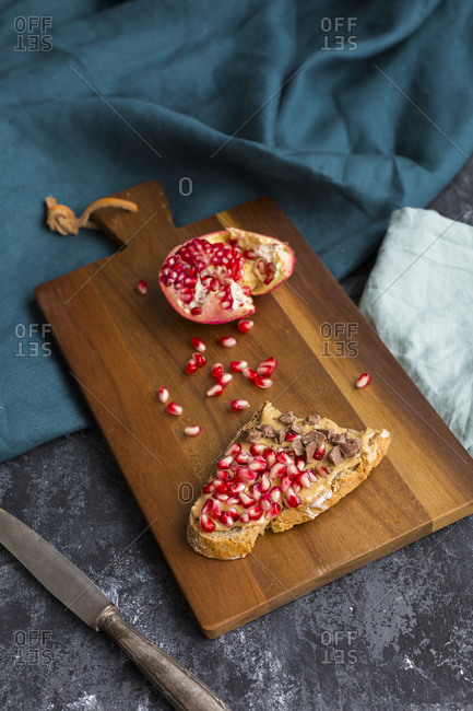 Slice of bread with peanut butter- pomegranate seed and chocolate pieces on wooden board