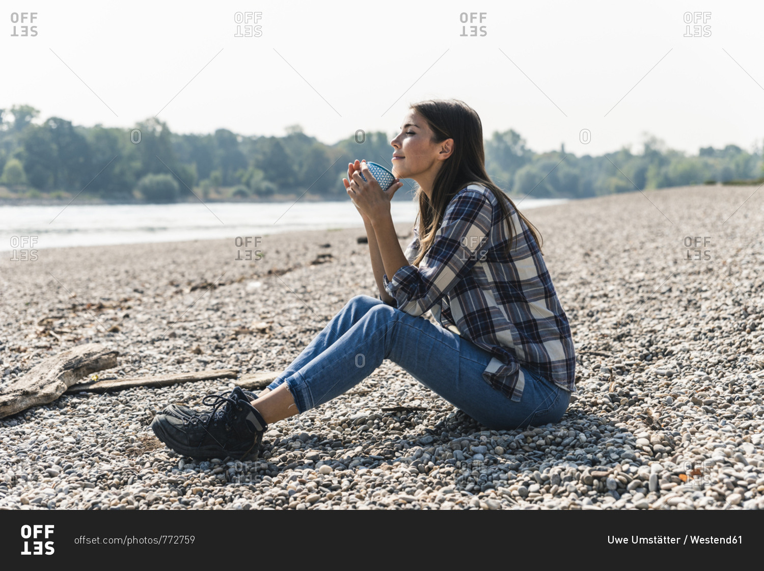 Relaxed young woman holding a mug sitting at the riverside