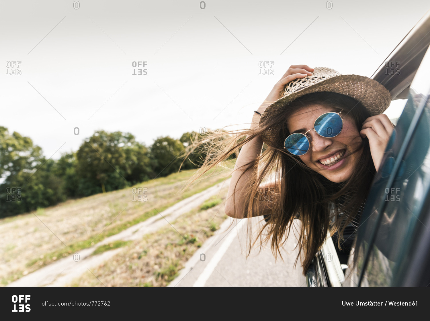 Happy young woman leaning out of car window