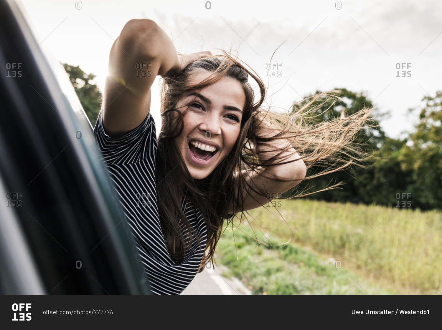 Carefree young woman leaning out of car window