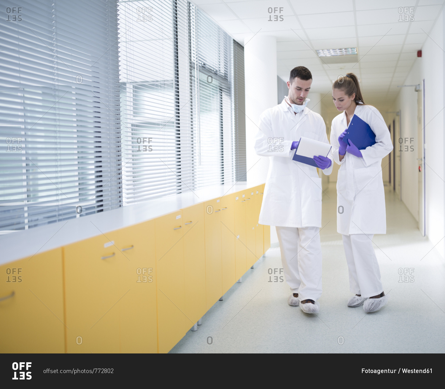 Man and woman in lab coats discussing on hallway