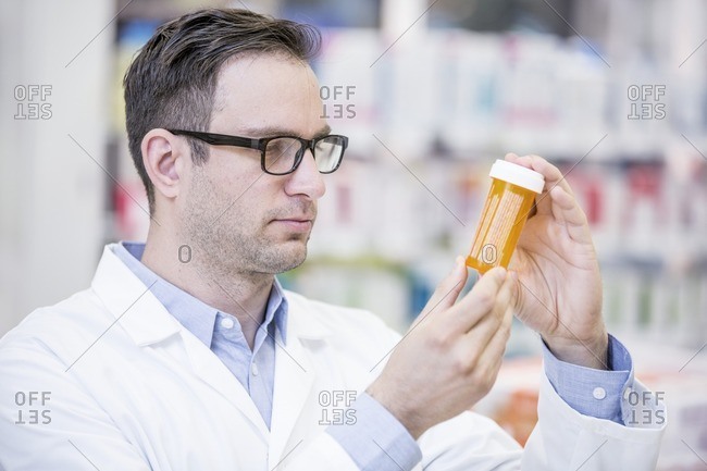 Male pharmacist reading label on pill bottle in pharmacy.