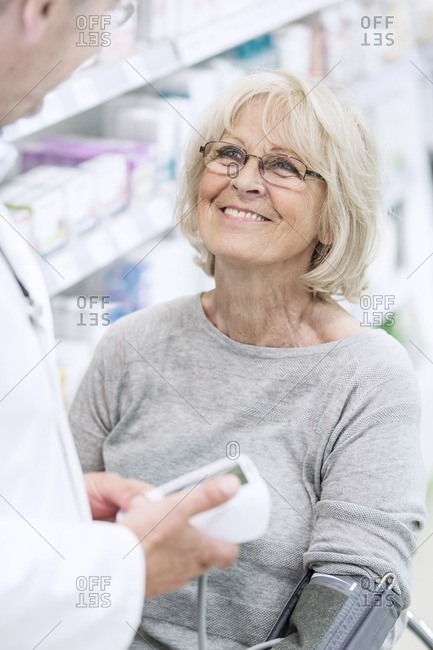 Male pharmacist checking smiling senior female patient's blood pressure in pharmacy.