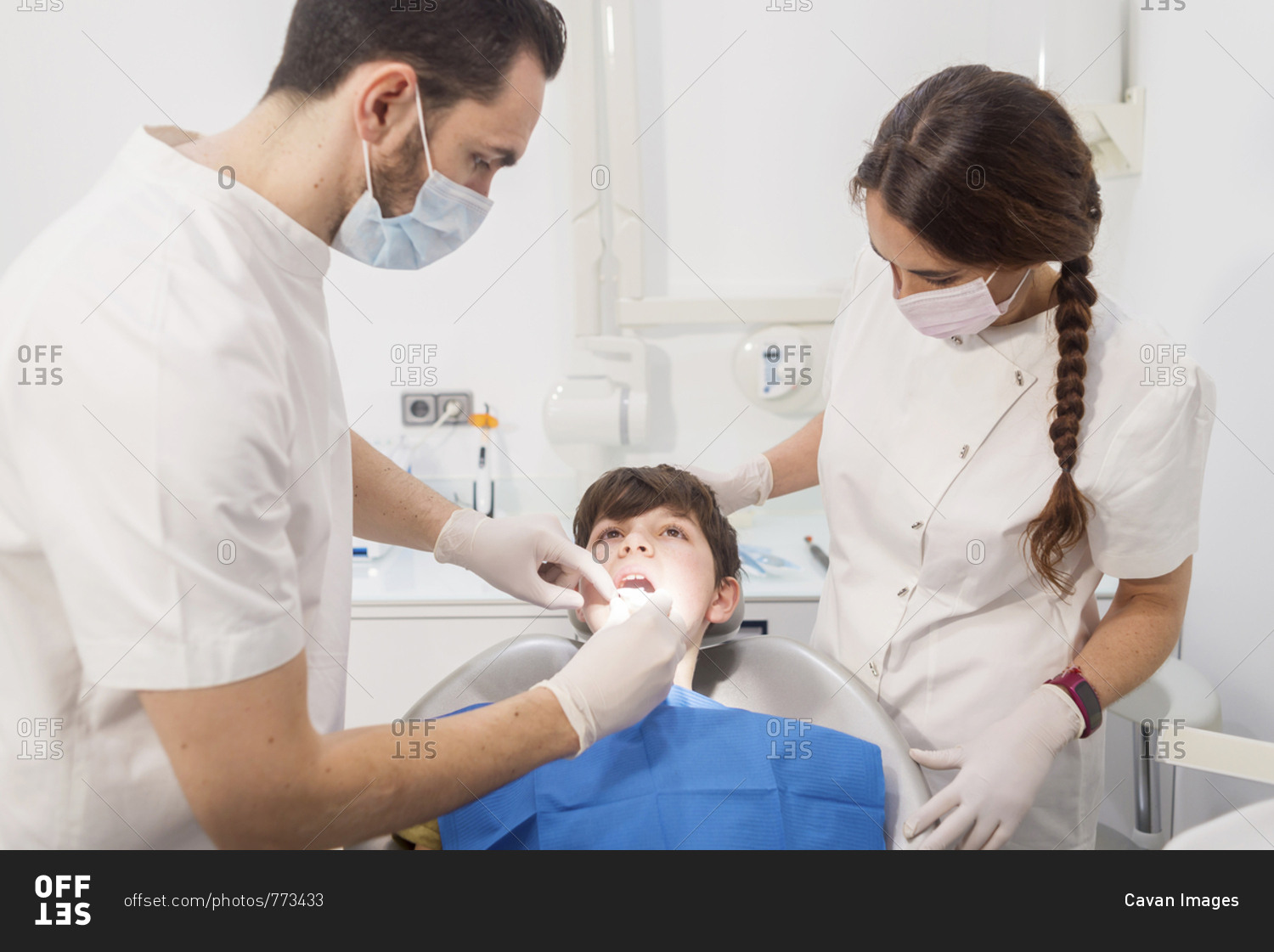Dentist examining patient's teeth by assistant in medical clinic