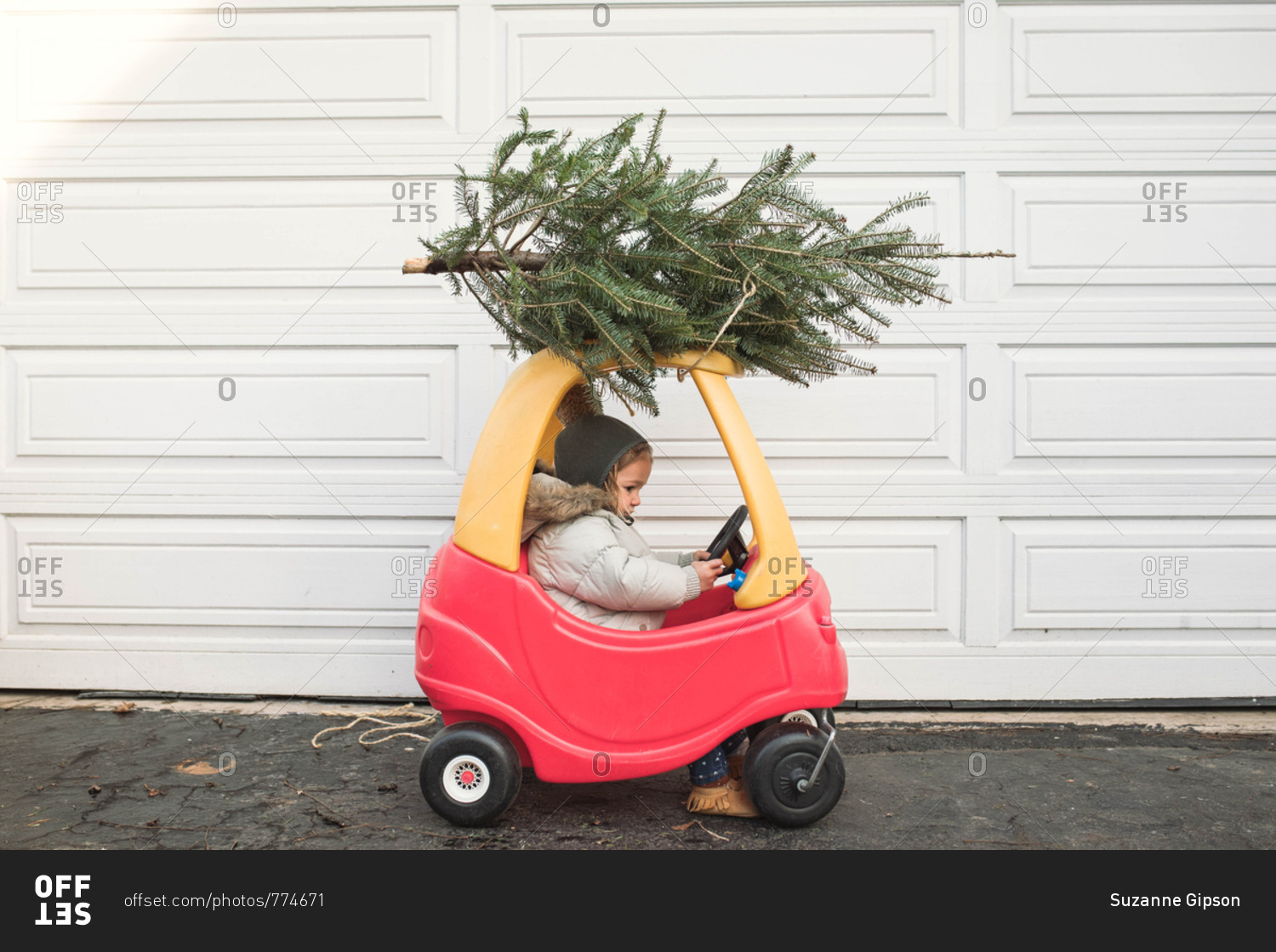 Side view of a child driving a toy car with a small Christmas tree